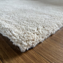 Detailfoto van een handgeknoopt Berber tapijt in crèmekleur, met zicht op de dikke wollen pool en fijne structuur. Hoogpolig vloerkleed van 100% zuivere scheerwol, liggend op een houten vloer – verkrijgbaar bij TTM Wonen voor een warm en natuurlijk interieur.